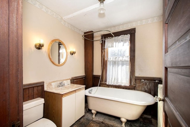 full bath with vanity, stone finish floor, a freestanding tub, and wainscoting