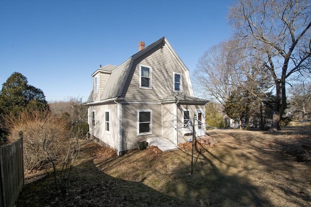 back of property with a gambrel roof, a chimney, and a shingled roof