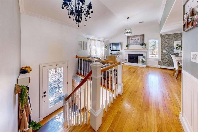 interior space with light wood finished floors, crown molding, lofted ceiling, a notable chandelier, and a glass covered fireplace