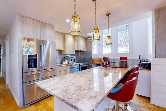 kitchen with light wood-type flooring, a breakfast bar, pendant lighting, light stone counters, and stainless steel appliances