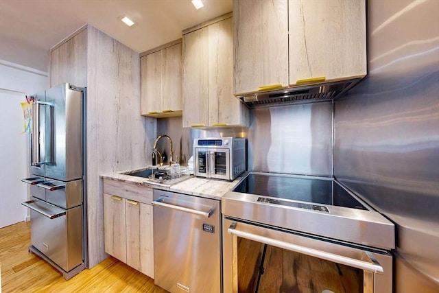 kitchen with light brown cabinets, a sink, stainless steel appliances, light wood-style floors, and light stone countertops