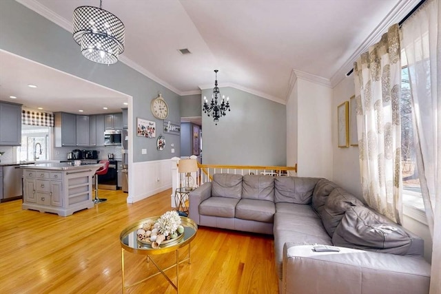 living room featuring a chandelier, wainscoting, light wood-style flooring, and vaulted ceiling