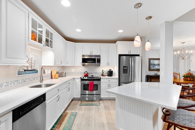 kitchen featuring hanging light fixtures, stainless steel appliances, sink, a kitchen bar, and white cabinetry