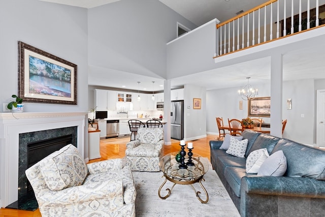 living room featuring a premium fireplace, light hardwood / wood-style flooring, an inviting chandelier, and a high ceiling