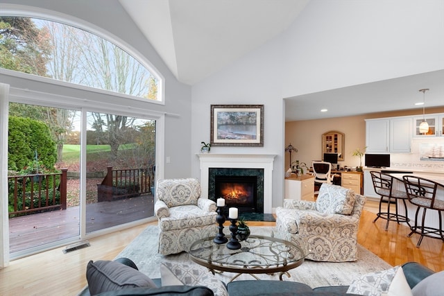 living room with high vaulted ceiling, a premium fireplace, and light hardwood / wood-style flooring