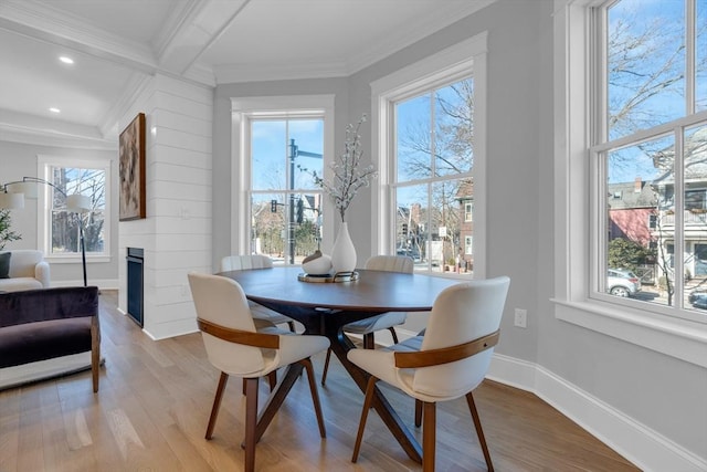 dining room with coffered ceiling, light wood-type flooring, a fireplace, ornamental molding, and beam ceiling