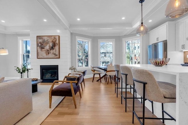 living room with a large fireplace, beamed ceiling, crown molding, and light hardwood / wood-style floors