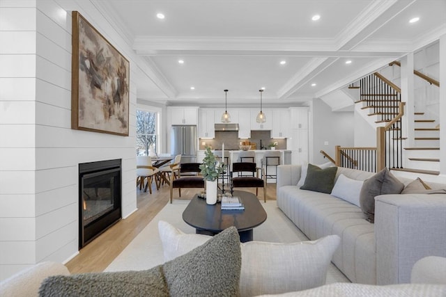 living room featuring ornamental molding, a large fireplace, light hardwood / wood-style flooring, and beam ceiling