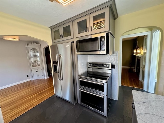 167 Pleasant St, East Longmeadow, MA 01028 - kitchen with appliances with stainless steel finishes, arched walkways, tasteful backsplash, glass insert cabinets, and baseboards