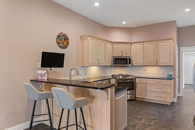 kitchen with light brown cabinets, stainless steel appliances, a peninsula, decorative backsplash, and a kitchen bar