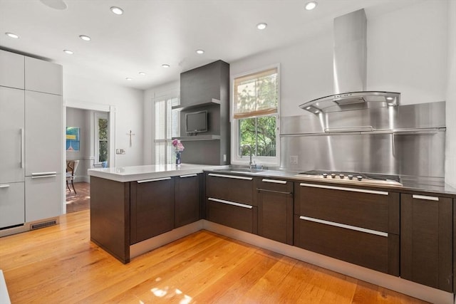 kitchen with modern cabinets, range hood, a peninsula, light wood-style flooring, and dark brown cabinetry