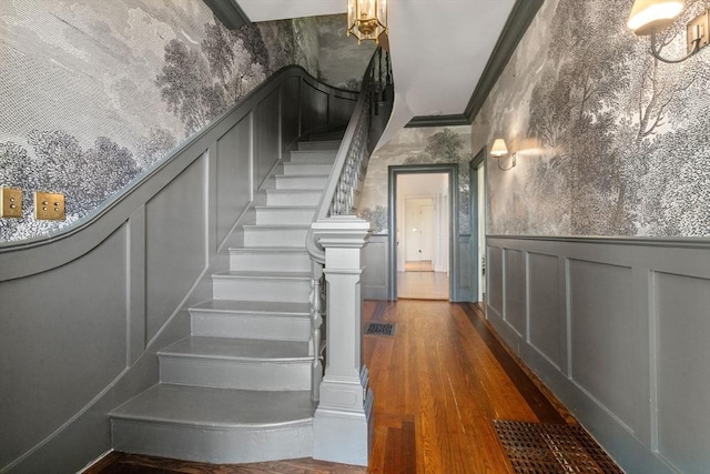 stairs with a decorative wall, wood finished floors, a wainscoted wall, and ornamental molding