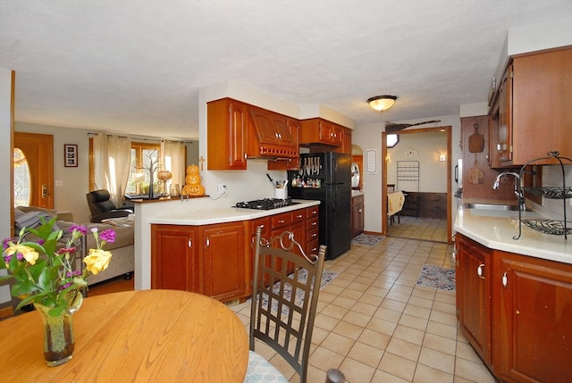 kitchen featuring sink, gas stovetop, kitchen peninsula, black refrigerator, and light tile patterned flooring