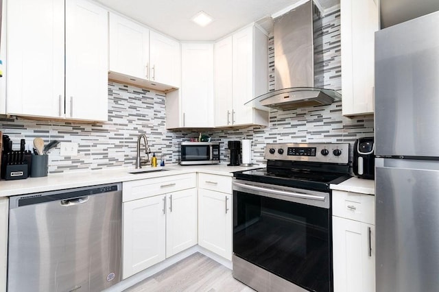 kitchen featuring appliances with stainless steel finishes, white cabinets, wall chimney range hood, and backsplash