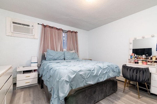 bedroom featuring light wood-type flooring, a wall mounted air conditioner, and a textured ceiling