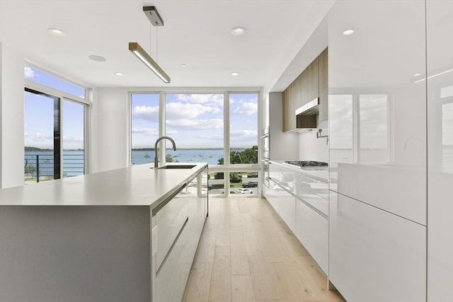 kitchen featuring sink, expansive windows, stainless steel gas stovetop, a kitchen island with sink, and a water view