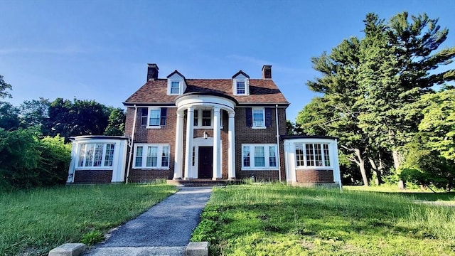 view of front of home featuring brick siding, a chimney, and a front lawn