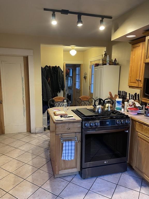 kitchen featuring brown cabinetry, light countertops, stainless steel gas stove, and light tile patterned flooring