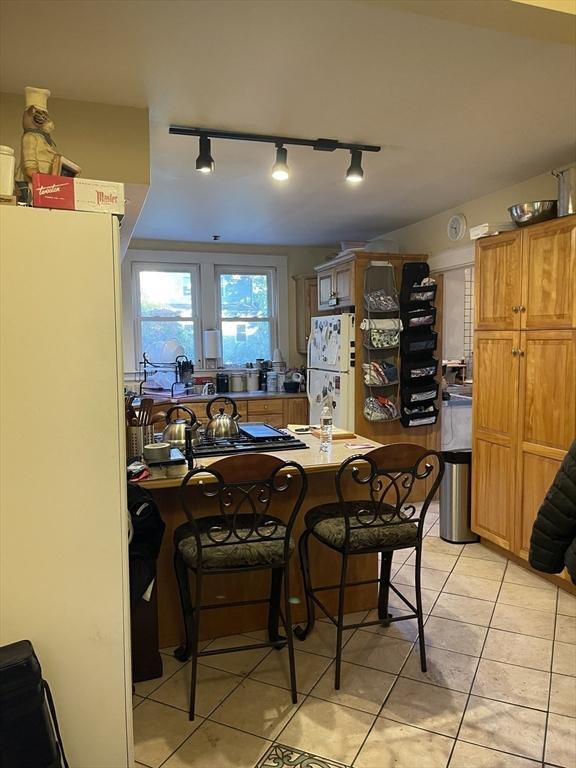 kitchen featuring light tile patterned floors, brown cabinetry, a kitchen bar, and freestanding refrigerator