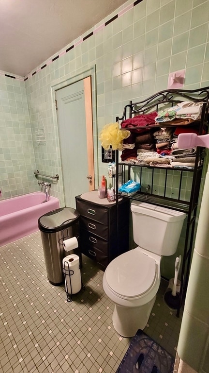 bathroom featuring toilet, tile patterned flooring, a washtub, and tile walls