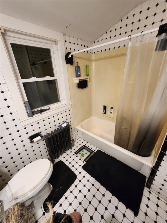 bathroom with tile walls, radiator, shower / bath combo with shower curtain, and toilet