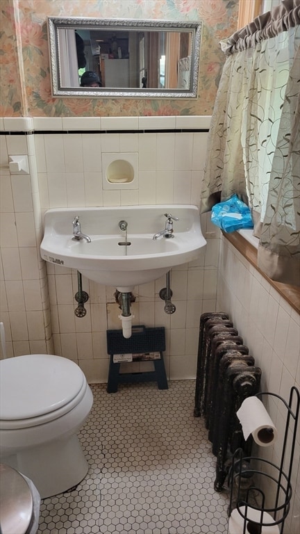 half bathroom featuring wallpapered walls, tile walls, and a wainscoted wall