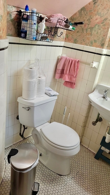 half bath featuring wallpapered walls, wainscoting, toilet, tile patterned floors, and tile walls