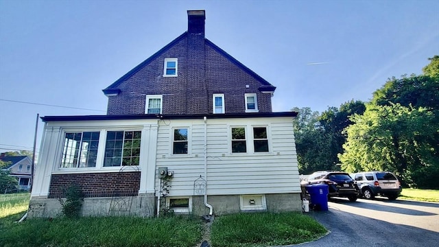 view of side of property with driveway, a chimney, and brick siding