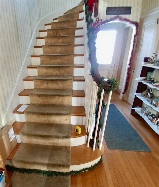 stairway featuring arched walkways, wood finished floors, and wallpapered walls