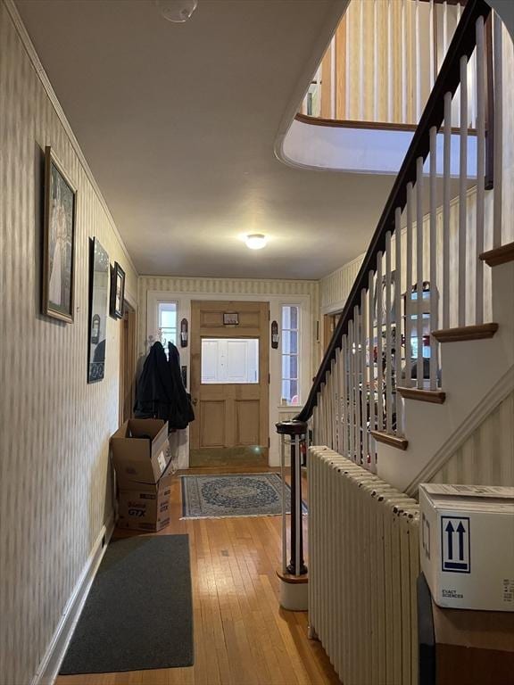 foyer entrance featuring stairs, radiator, wallpapered walls, and wood finished floors