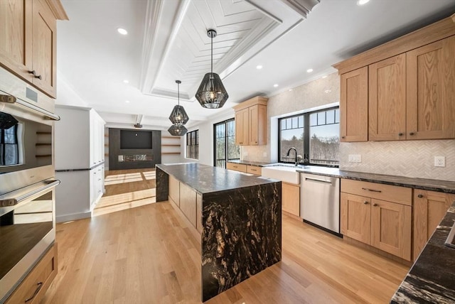 kitchen with decorative light fixtures, stainless steel appliances, sink, light wood-type flooring, and a tray ceiling