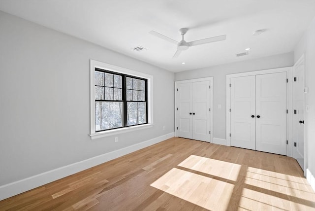 unfurnished bedroom with multiple closets, light hardwood / wood-style floors, and ceiling fan