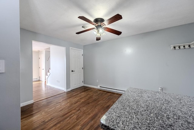 interior space with dark wood-type flooring, ceiling fan, and a baseboard heating unit