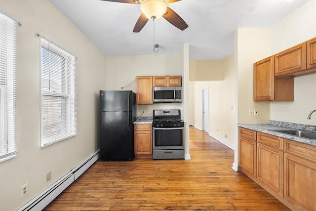 kitchen with ceiling fan, sink, baseboard heating, light hardwood / wood-style flooring, and appliances with stainless steel finishes