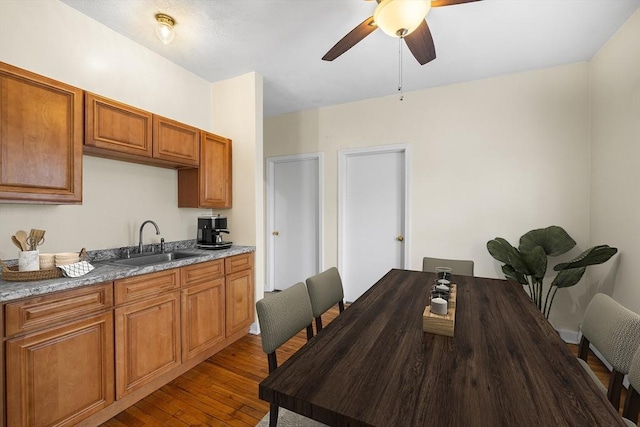 kitchen with hardwood / wood-style floors, ceiling fan, light stone counters, and sink