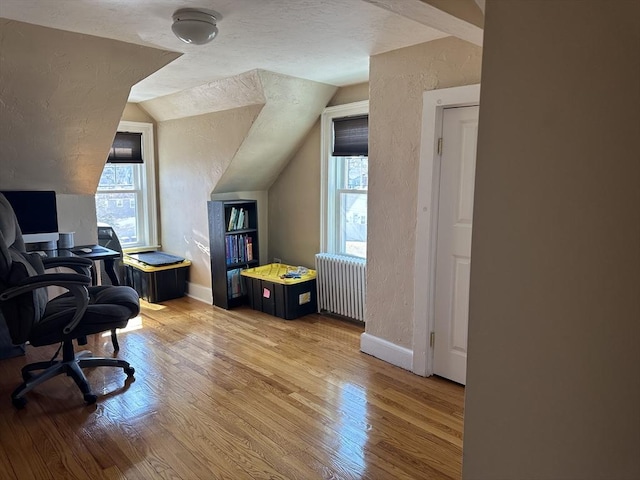 office area with lofted ceiling, radiator heating unit, light wood-style flooring, and a textured wall