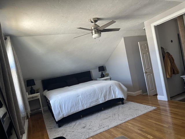 bedroom with a textured ceiling, wood finished floors, a ceiling fan, baseboards, and vaulted ceiling