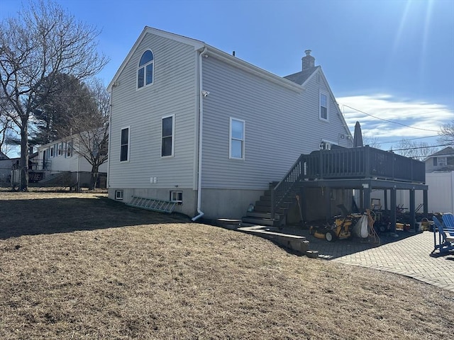 view of side of home featuring a patio, a chimney, a lawn, stairway, and a wooden deck