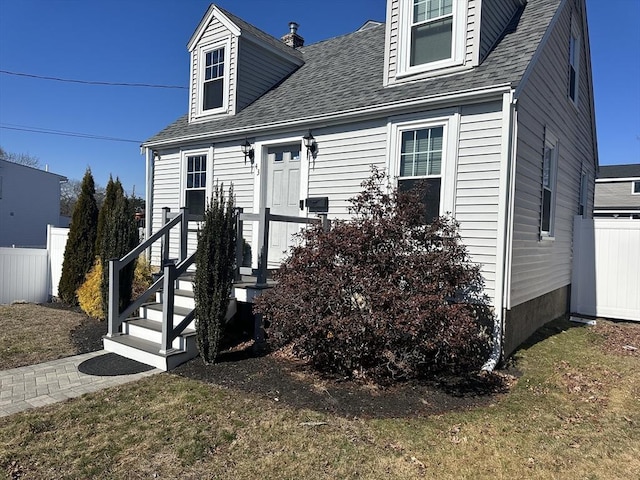 cape cod home with a shingled roof, fence, and a front yard