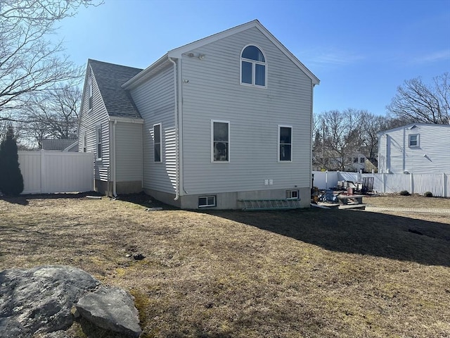 rear view of house featuring roof with shingles, fence, and a lawn