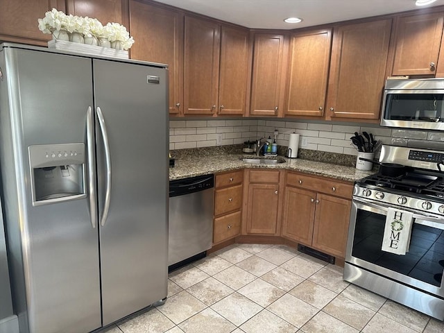 kitchen with dark stone countertops, a sink, stainless steel appliances, backsplash, and light tile patterned flooring