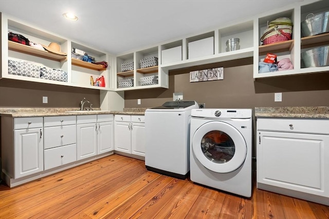 washroom with a sink, washer and clothes dryer, cabinet space, and light wood finished floors