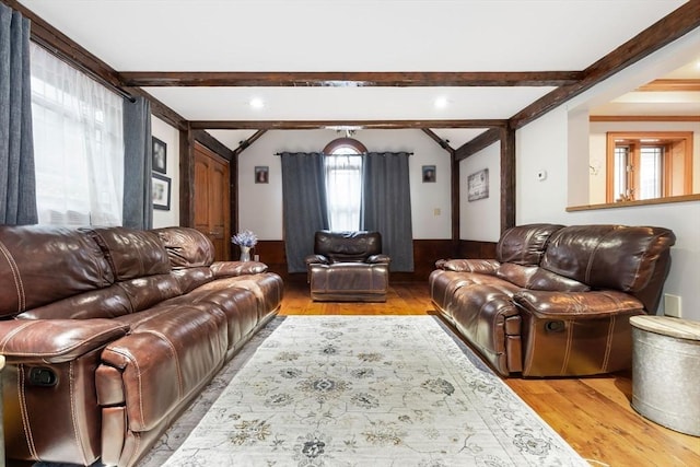 living room featuring light wood-style floors, beamed ceiling, and wainscoting