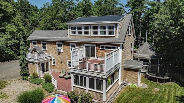 rear view of property featuring a trampoline, a shingled roof, cooling unit, and a balcony