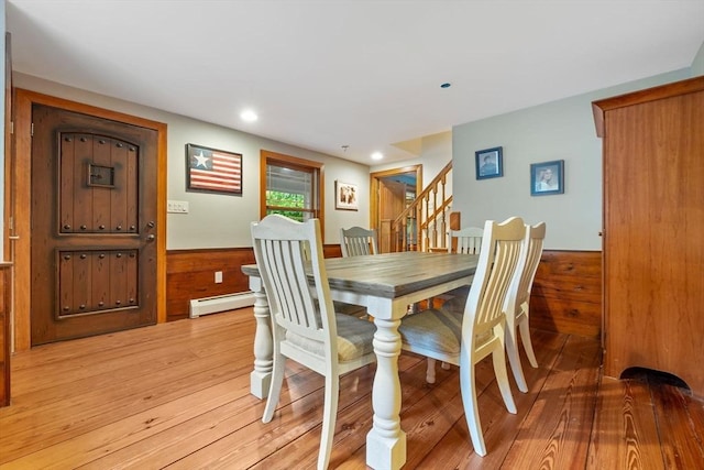 dining room with stairs, wood walls, a wainscoted wall, and light wood-style floors