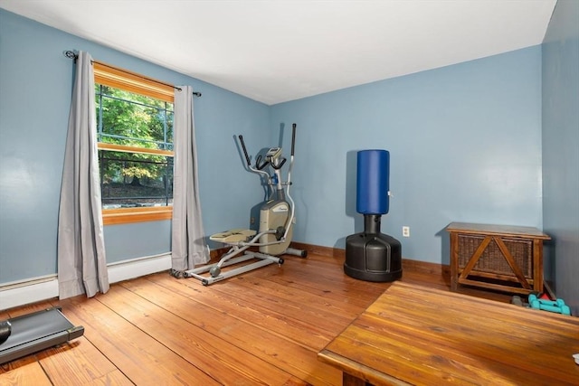 workout room featuring baseboards, a baseboard heating unit, and wood finished floors