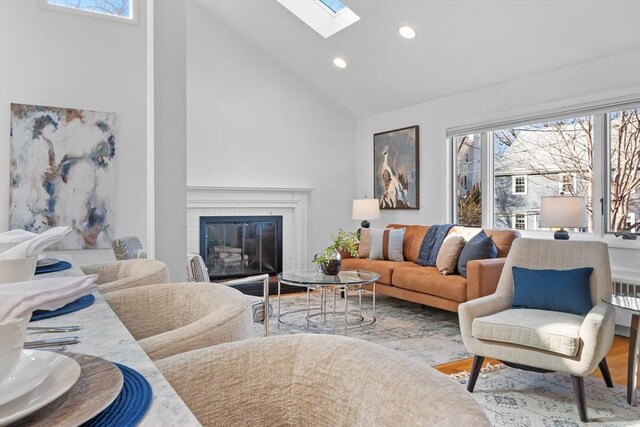 living area with high vaulted ceiling, wood finished floors, recessed lighting, a skylight, and a brick fireplace