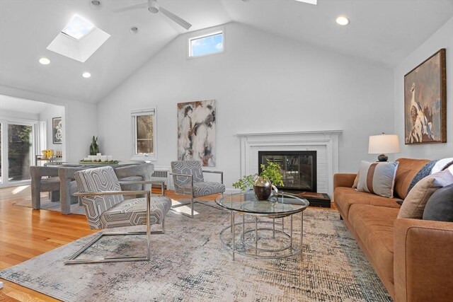 living room with ceiling fan, a fireplace, a skylight, wood finished floors, and high vaulted ceiling