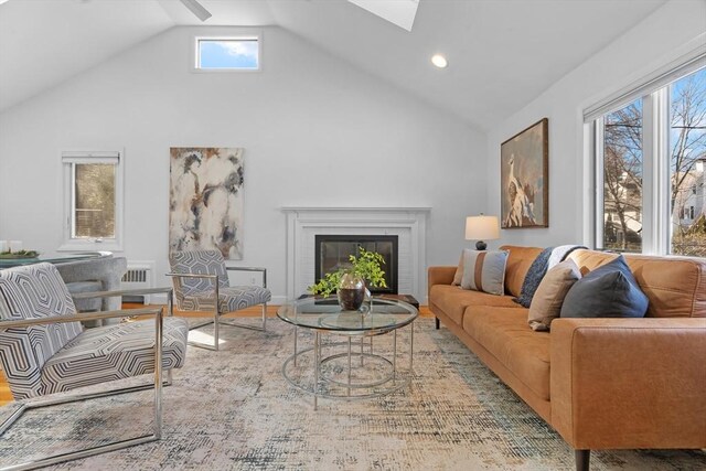 living area with a wealth of natural light, a glass covered fireplace, and lofted ceiling with skylight
