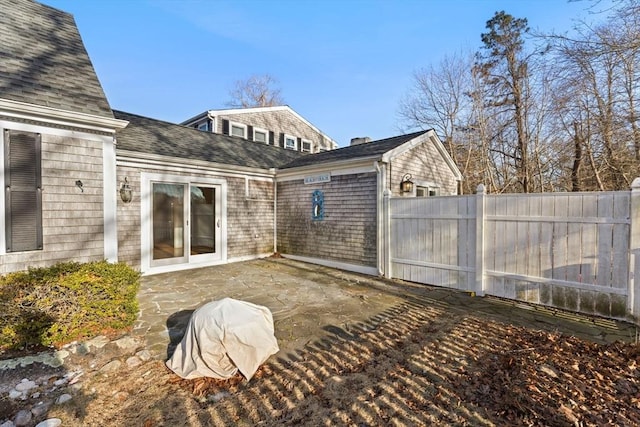 back of house with a shingled roof, a patio, and fence